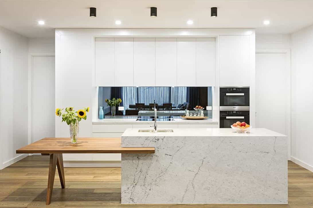 Modern minimalist kitchen in Mont Albert with white handleless cabinetry, stone island and timber table