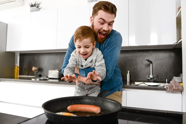 Cheerful Bearded Father Cooking At Kitchen With His Little Son