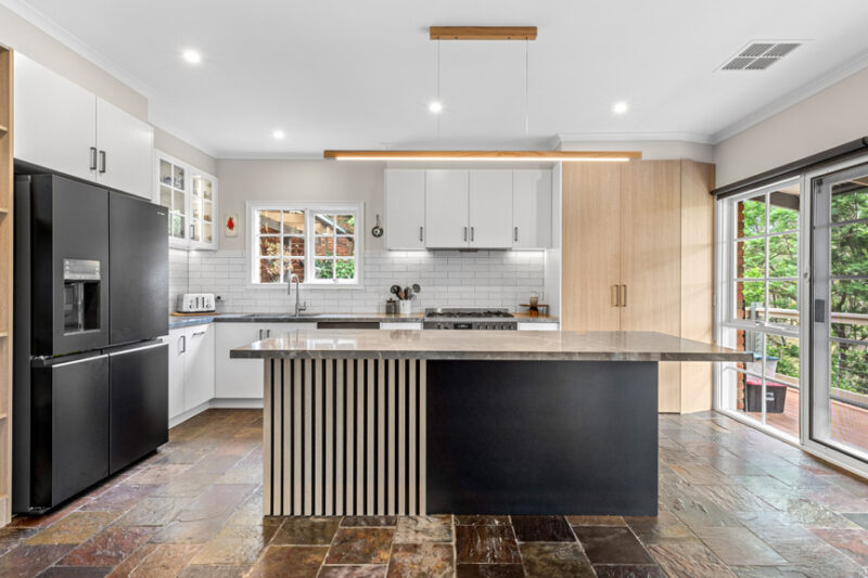 Transitional kitchen renovation in Templestowe with black island, timber feature panels and white cabinetry