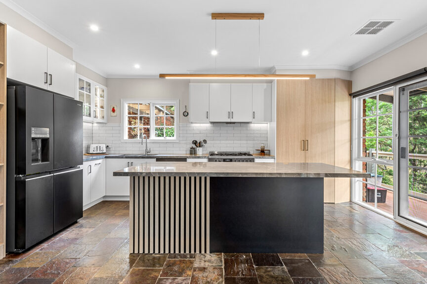 Transitional kitchen renovation in Templestowe with black island, timber feature panels and white cabinetry